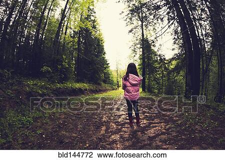 Stock Image - Caucasian girl walking on dirt path in forest. Fotosearch