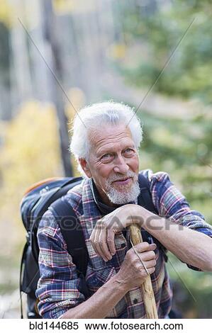 Stock Photography - Caucasian hiker leaning on walking stick in forest. Fotosearch