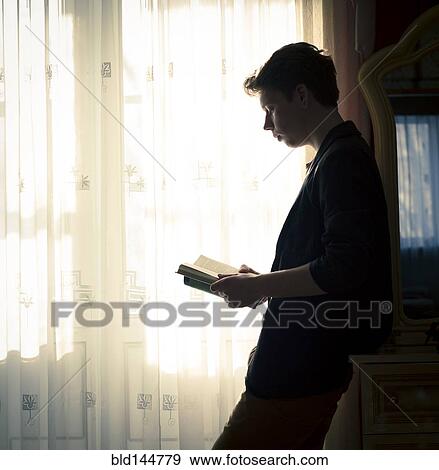 Stock Photo - Caucasian man reading book near window. Fotosearch