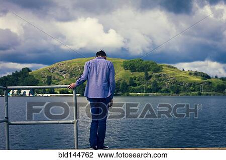 Stock Image - Caucasian man standing on dock at lake. Fotosearch