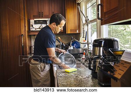 Stock Image - Caucasian man washing dishes in kitchen. Fotosearch