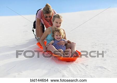 Picture - Caucasian mother and children sledding on sand dune. Fotosearch