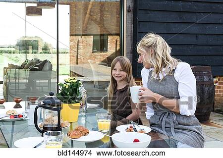 Picture - Caucasian mother and daughter having breakfast in backyard. Fotosearch
