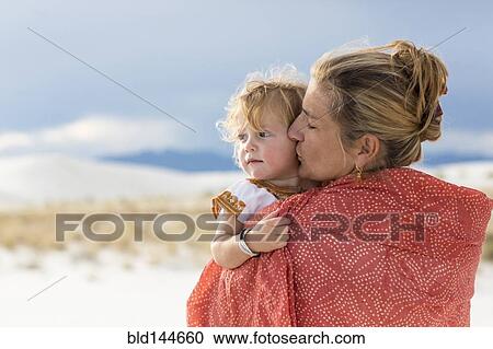 Stock Image - Caucasian mother and son wrapped in blanket on sand dune. Fotosearch