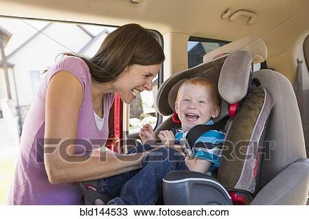 Stock Image - Caucasian mother fastening son into car seat. Fotosearch