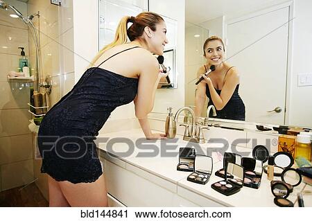 Stock Image - Caucasian woman applying makeup in bathroom mirror. Fotosearch