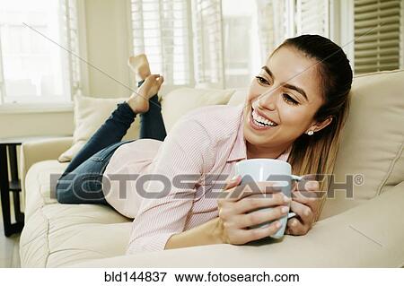 Stock Photo - Caucasian woman drinking cup of coffee on sofa. Fotosearch