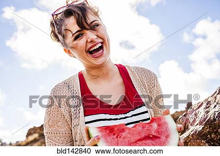 Stock Image - Caucasian woman eating watermelon outdoors. Fotosearch