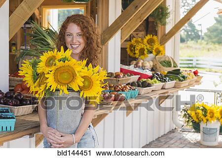Stock Image - Caucasian woman holding sunflowers at farmers market. Fotosearch