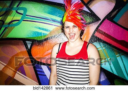 Stock Image - Caucasian woman in colorful wig laughing near graffiti wall. Fotosearch