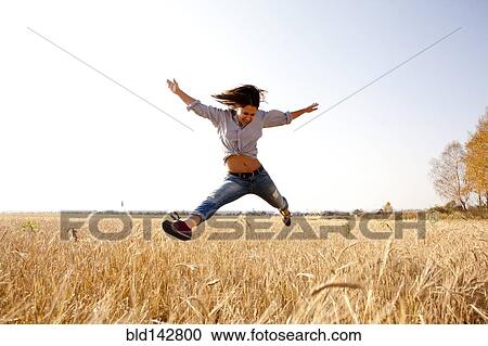 Stock Image - Caucasian woman jumping for joy in rural field. Fotosearch