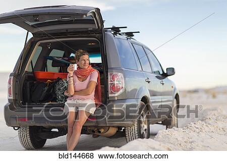 Caucasian woman leaning on car drinking coffee View Large Photo Image Stock Photo - Caucasian woman leaning on car drinking coffee. Fotosearch