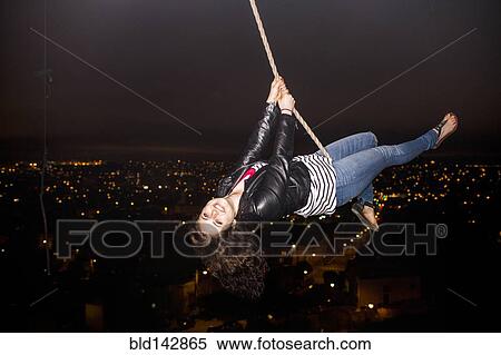 Stock Photography - Caucasian woman on rope swinging over scenic view of cityscape. Fotosearch