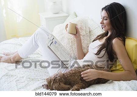 Stock Photo - Caucasian woman reading magazine with pet dog in bed. Fotosearch