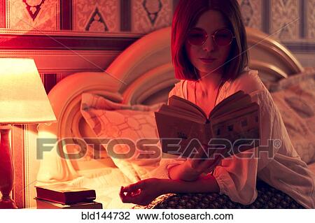 Stock Image - Caucasian woman reading on bed. Fotosearch