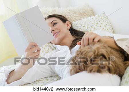 Stock Image - Caucasian woman reading with pet dog. Fotosearch
