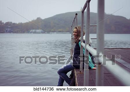 Stock Photograph - Caucasian woman sitting on dock over still lake. Fotosearch