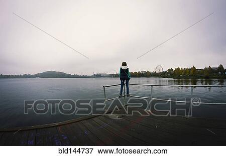 Stock Photo - Caucasian woman standing on dock over still lake. Fotosearch