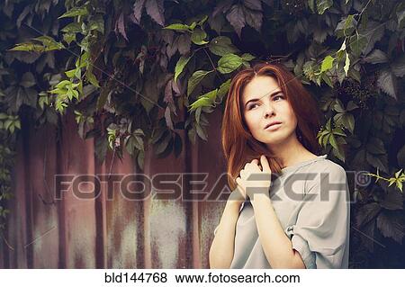 Stock Photo - Caucasian woman standing under leaves by fence. Fotosearch