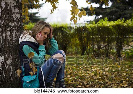 Stock Photography - Caucasian woman talking on cell phone near tree. Fotosearch