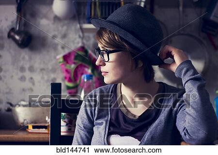 Stock Image - Caucasian woman wearing hat and eyeglasses in kitchen. Fotosearch