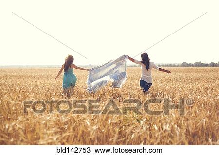 Stock Image - Caucasian women carrying blanket in rural field. Fotosearch