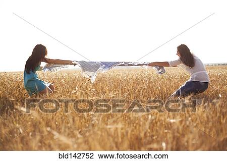 Stock Image - Caucasian women playing tug-of-war in rural field. Fotosearch