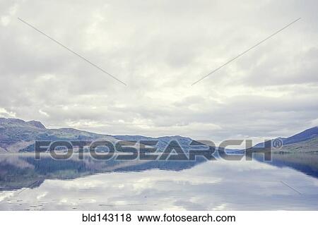 Cloudy sky and hilly landscape reflected in still lake View Large Photo Image Stock Photo - Cloudy sky and hilly landscape reflected in still lake. Fotosearch