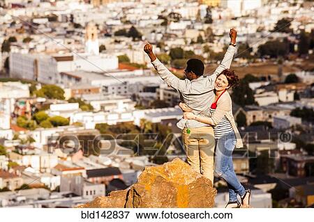 Stock Photo - Couple cheering near scenic view of cityscape. Fotosearch