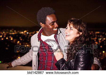 Couple hugging near scenic view of cityscape at night View Large Photo Image Stock Photo - Couple hugging near scenic view of cityscape at night. Fotosearch