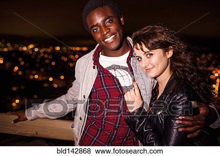 Couple hugging near scenic view of cityscape at night View Large Photo Image Stock Photo - Couple hugging near scenic view of cityscape at night. Fotosearch