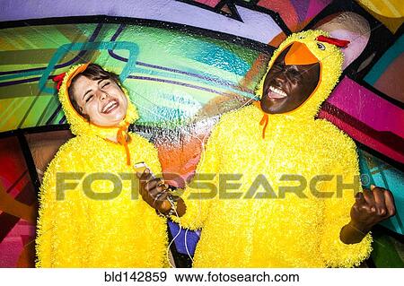 Stock Photo - Couple in identical costumes listening to earbuds near graffiti wall. Fotosearch