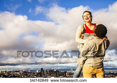 Stock Photo - Couple laughing near scenic view of cityscape. Fotosearch