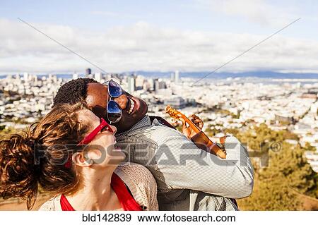 Stock Photo - Couple playing ukulele near scenic view of cityscape. Fotosearch