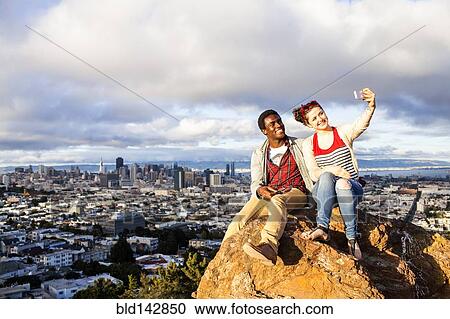 Couple taking cell phone selfie on rock overlooking cityscape View Large Photo Image Stock Image - Couple taking cell phone selfie on rock overlooking cityscape. Fotosearch