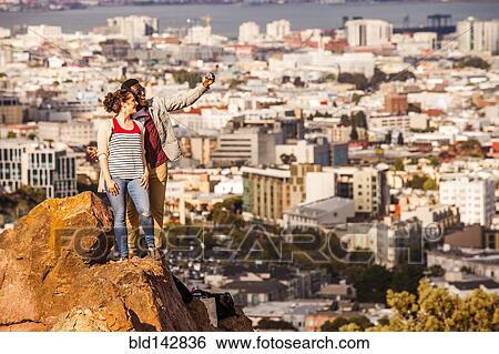 Couple taking cell phone selfie on rock overlooking scenic view of cityscape View Large Photo Image Stock Photograph - Couple taking cell phone selfie on rock overlooking scenic view of cityscape. Fotosearch