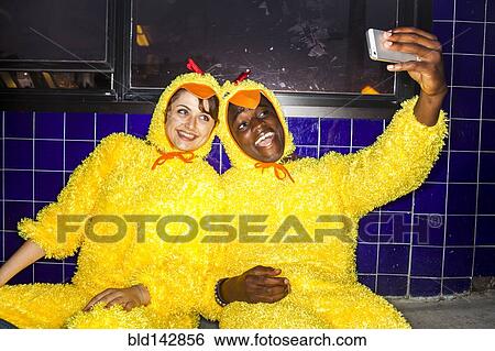 Stock Photograph - Couple taking cell phone selfies wearing chicken costumes . Fotosearch