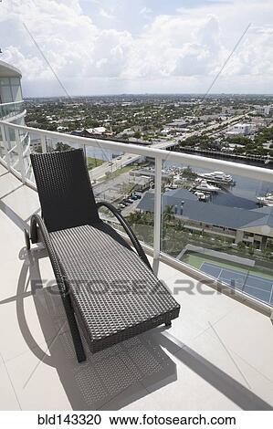 Stock Image - Deck chair on balcony overlooking cityscape. Fotosearch