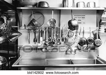 Stock Image - Dishes hanging above commercial kitchen sink. Fotosearch
