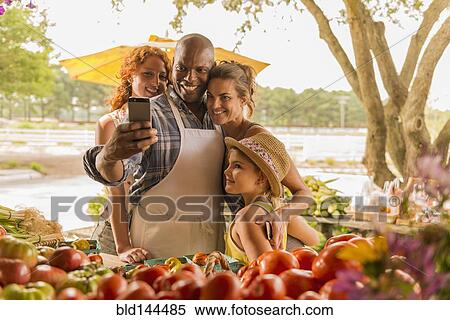Stock Photography - Family taking cell phone selfie at farmers market. Fotosearch