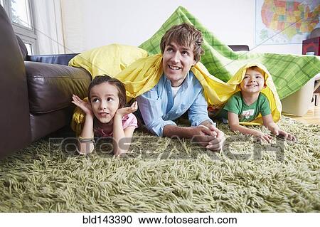 Stock Image - Father and children playing in blanket fort in living room. Fotosearch