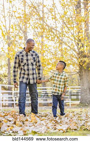 Stock Photo - Father and son holding hands in autumn leaves. Fotosearch