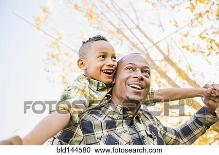 Stock Image - Father carrying son outdoors. Fotosearch