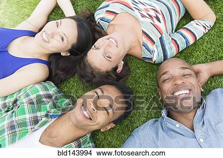 Picture - Friends laying in grass outdoors. Fotosearch
