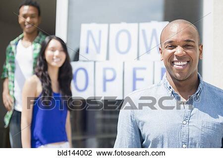 Stock Image - Friends smiling together by newly open storefront. Fotosearch