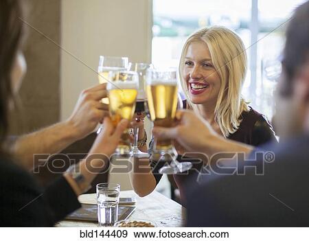 Stock Photo - Friends toasting with beer in cafe. Fotosearch