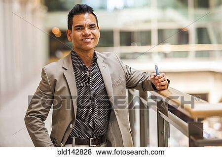 Stock Photo - Hispanic businessman holding cell phone near banister. Fotosearch
