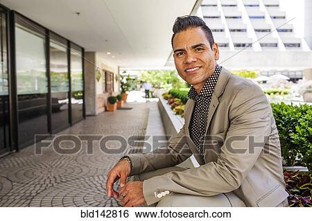 Stock Photograph - Hispanic businessman leaning over outdoor bench. Fotosearch