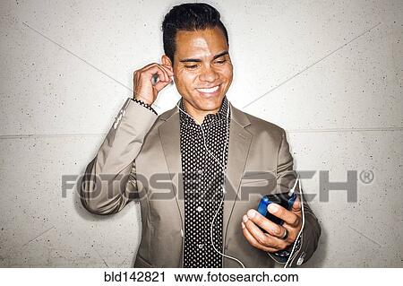 Stock Image - Hispanic businessman listening to earbuds with cell phone. Fotosearch