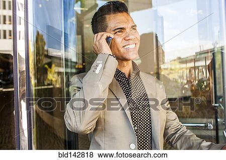 Stock Photo - Hispanic businessman talking on cell phone near window. Fotosearch